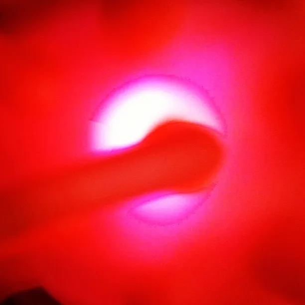 An abstract close-up image featuring a glowing white and pink circular light source with a red gradient, partially obscured by a translucent cylindrical object.