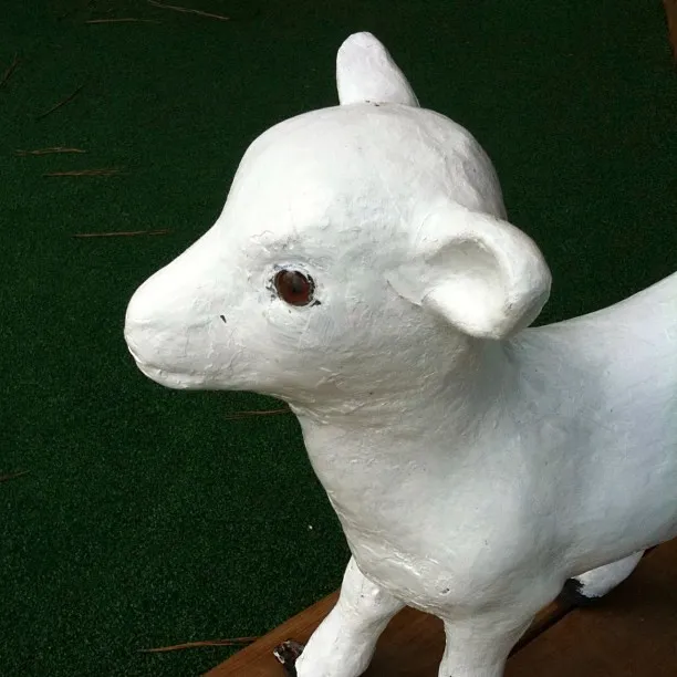 Close-up of a white-painted lamb or goat sculpture with a smooth surface, standing on artificial green grass.