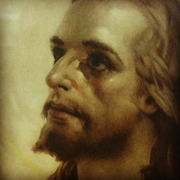 Close-up of a traditional-style painting showing a bearded man with long hair gazing upward, rendered in warm, soft tones.