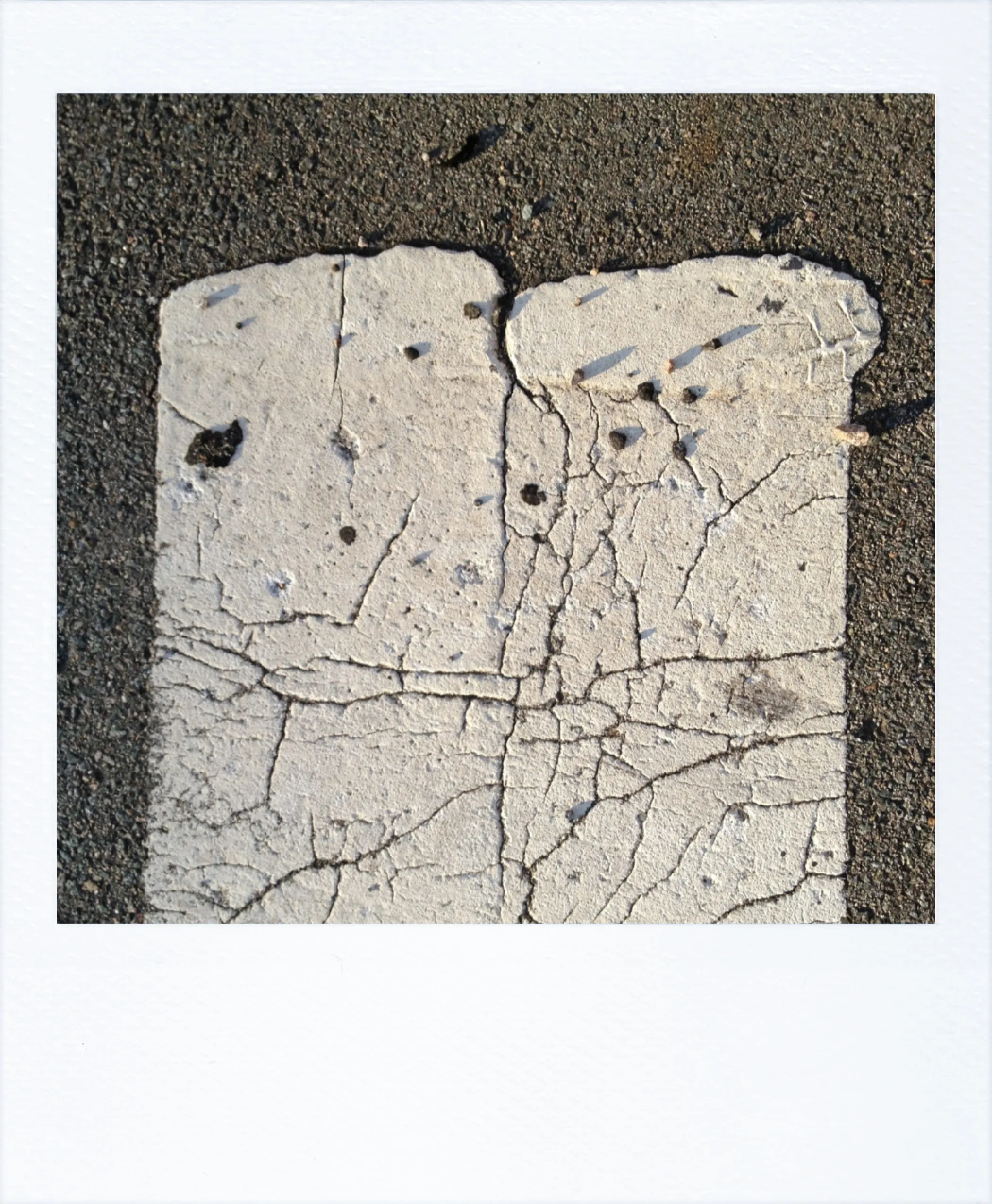 Close-up of two adjacent, cracked white pavement markings with a small gap between them on dark asphalt.
