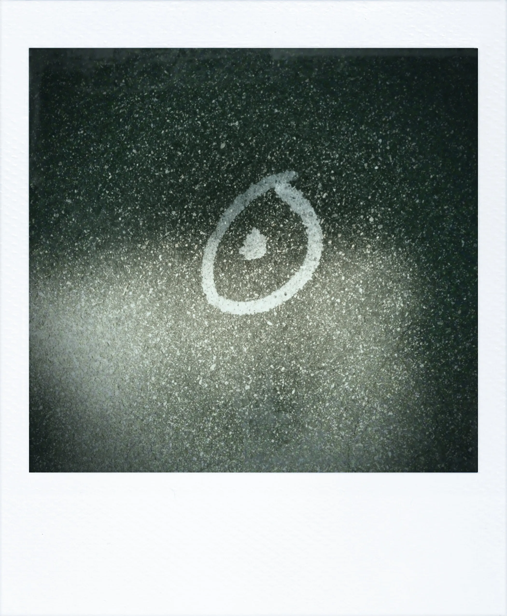 Spray-painted circle with a dot in the center on dark speckled asphalt, resembling a crude symbol or mark.